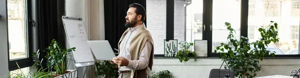 An elderly handsome man stands thoughtfully in a modern office, surrounded by plants and light. — Stock Photo