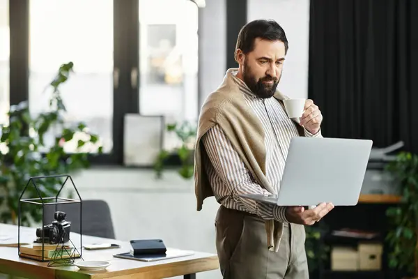 An attractive senior man savors a cup of coffee as he focuses on his laptop in a cozy workspace. — Stock Photo