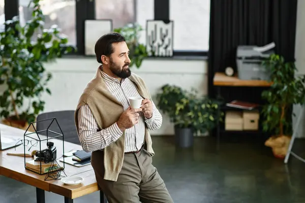 Handsome senior man holds a cup of coffee, relaxing in a chic office filled with plants. — Stock Photo
