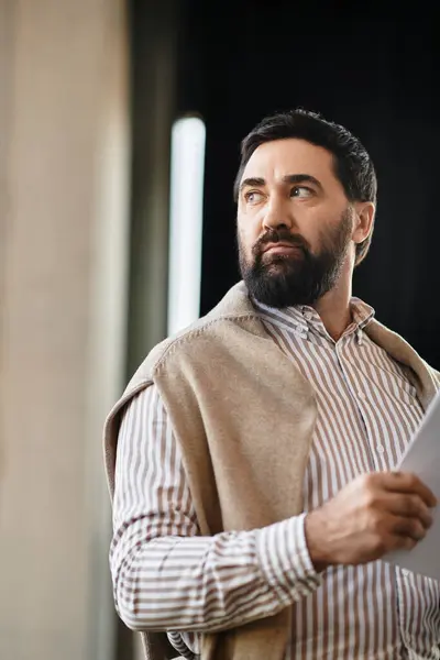 Un bell'uomo anziano con la barba sta in casa, guardando attentamente un pezzo di carta.. — Stock Photo
