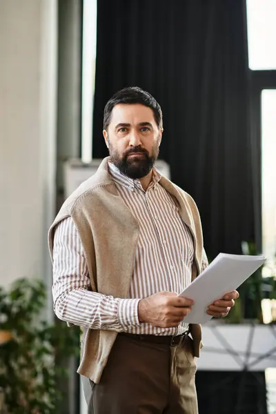 An attractive senior man stands with papers, quietly pondering in a modern, spacious room. — Stock Photo
