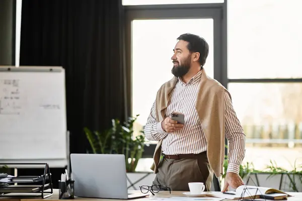 Ein älterer Herr steht lässig in einem hellen Büro und lächelt mit seinem Smartphone in der Hand.. — Stockfoto