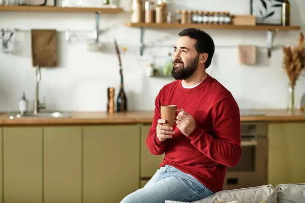 A handsome senior man relaxes with a warm beverage, savoring moments in a stylish kitchen. — Stock Photo
