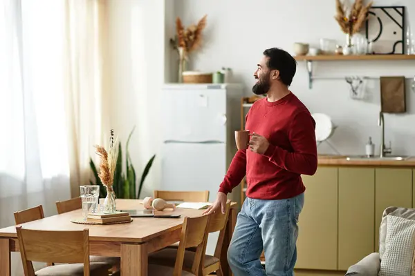 Elderly man enjoys a warm drink by a sunlit window in a cozy kitchen. — Stock Photo