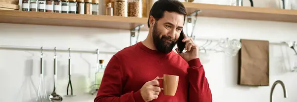 An elderly handsome man enjoys a cup of coffee while chatting on the phone in his cozy kitchen. — Stock Photo