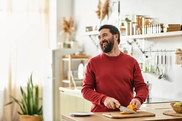 An attractive senior man smiles while chopping vibrant vegetables in a sunny kitchen space. — Stock Photo