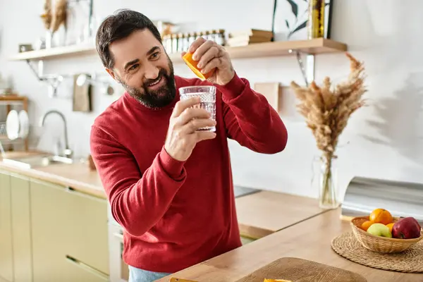 Handsome senior man creates a delightful beverage, adding fresh fruit in a warm, inviting kitchen. — Stock Photo