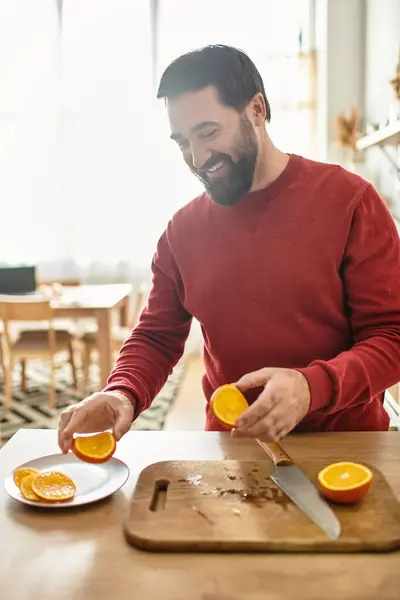 Handsome elderly man smiles while preparing fresh oranges on a sunny kitchen countertop. — Stock Photo