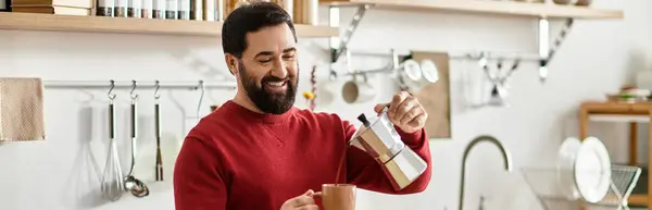 Hombre mayor guapo vierte café humeante en una taza mientras está de pie en una cocina acogedora. - foto de stock