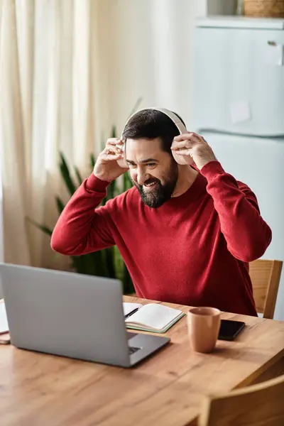 Uomo anziano in casual maglione rosso condivide un momento felice mentre si impegna online alla sua scrivania. — Foto stock