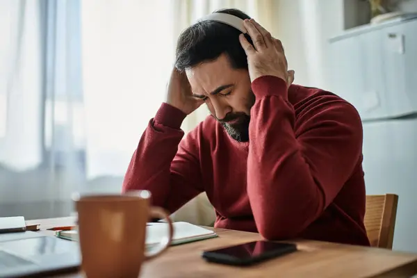 Handsome senior man listens to music with headphones, sitting at a wooden table in a bright room. — Stock Photo