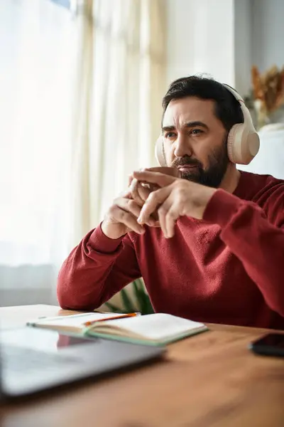 A handsome elderly man sits at a wooden table, lost in thought while enjoying music. — Stock Photo