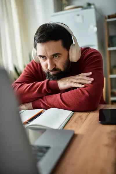 Ein älterer Mann sitzt gedankenverloren an einem Holztisch und hört mit Kopfhörern zu.. — Stockfoto