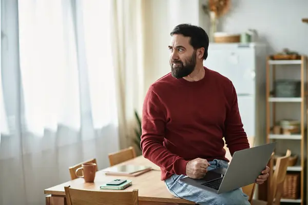 A handsome senior man in casual attire explores ideas on his laptop, bathed in natural light. — Stock Photo