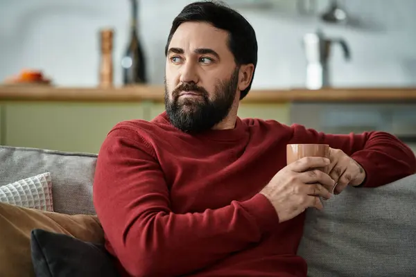 Schöner Senior entspannt sich auf einer Couch und genießt ein warmes Getränk, während er über das Leben nachdenkt. — Stockfoto
