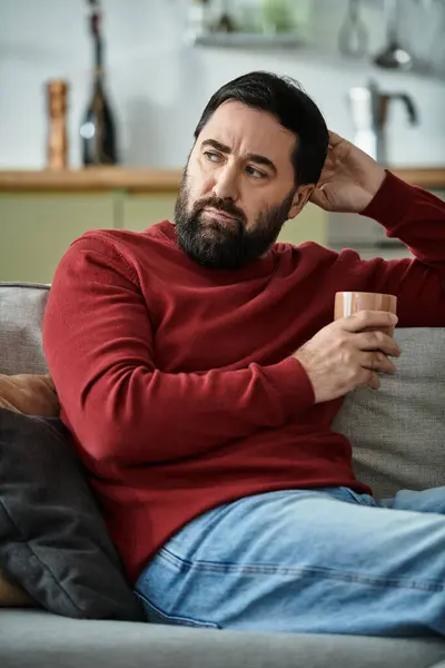 An elderly handsome gentleman relaxes on a couch, savoring his warm drink in a serene setting. — Stock Photo