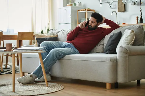 An elderly man is chatting casually on the phone while lounging on a cozy couch. — Stock Photo