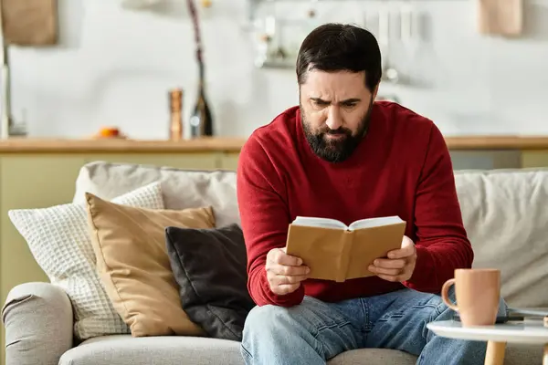 An elderly handsome man enjoys reading a book while comfortably seated in a cozy living space. — Stock Photo