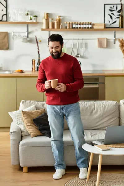 Senior man in a red sweater enjoys a warm drink in a cozy living space. — Stock Photo
