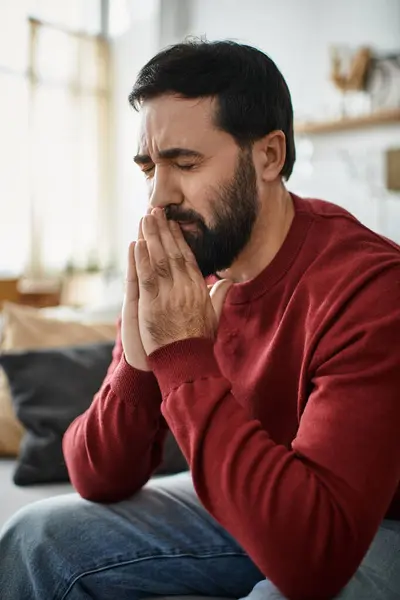 Un bell'uomo anziano siede pensieroso su un divano, immerso nel pensiero, in un salotto illuminato dal sole. — Foto stock