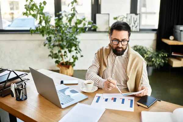 Good looking senior man reviews charts and graphs in a relaxed office setting while sipping coffee. — Stock Photo