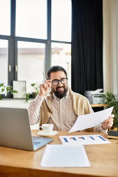 Un bell'uomo anziano con la barba si siede a una scrivania, analizza i rapporti e si gode un caffè. — Foto stock