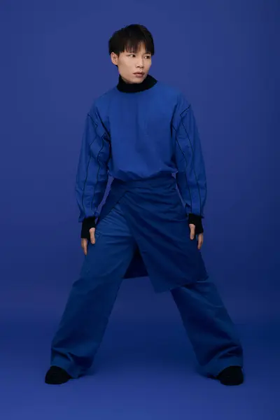 Guapo joven asiático hombre posa con confianza en un artístico traje azul sobre un rico telón de fondo. — Stock Photo