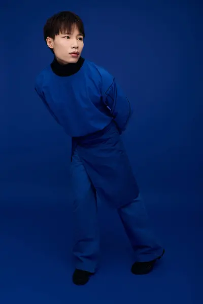 Un joven con estilo se levanta juguetonamente, rodeado de ricos tonos azules, mostrando su encanto. — Stock Photo
