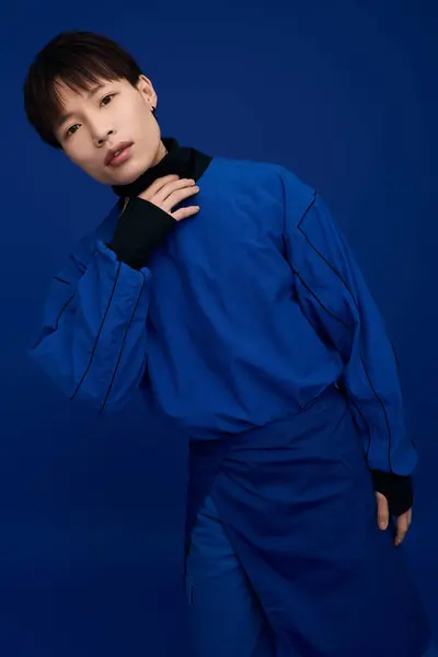 A young asian man stands gracefully in a striking blue outfit, showcasing modern fashion and charm. — Stock Photo