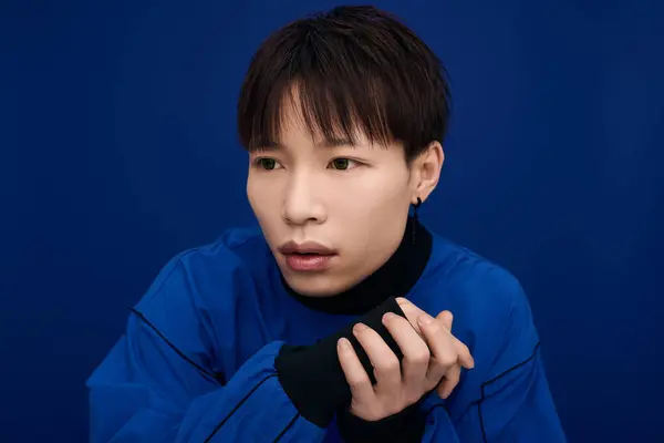 A young Asian man, deep in thought, has an expressive look against a vibrant blue backdrop. — Stock Photo