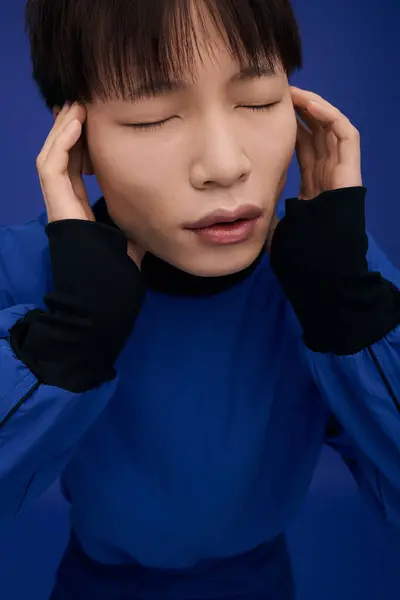 A handsome young Asian man with closed eyes displays deep emotion in a vivid blue setting. — Stock Photo