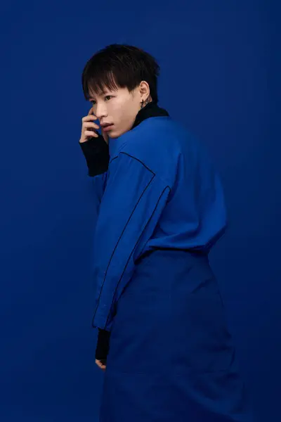 Attractive young Asian man stands elegantly, exuding charisma with a striking blue backdrop. — Stock Photo
