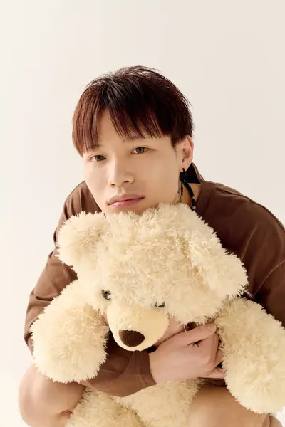 Un jeune homme étreint un ours en peluche, exsudant confort et joie dans un cadre minimaliste. — Photo de stock