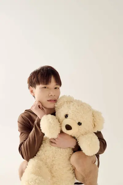 Un jeune homme asiatique attrayant tient doucement un ours en peluche doux, mettant en valeur la chaleur et l'innocence. — Photo de stock