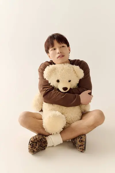 A good looking young man sits crossed legged, holding a fluffy teddy bear in a serene atmosphere. — Stock Photo