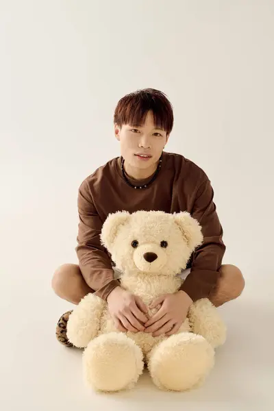 A charming young man shares a moment with a fluffy teddy bear indoors. — Stock Photo