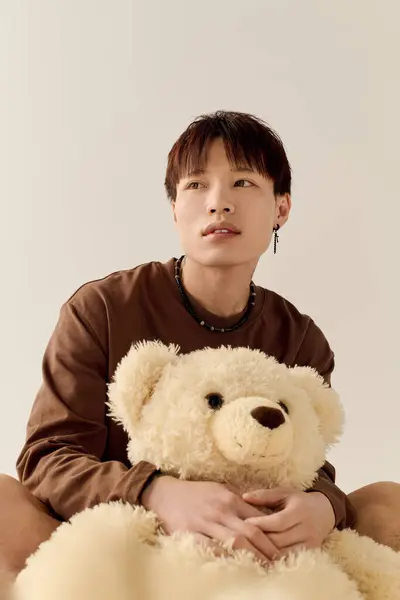 Jeune homme attrayant tient un ours en peluche confortable tout en regardant attentivement dans un espace intérieur calme. — Photo de stock