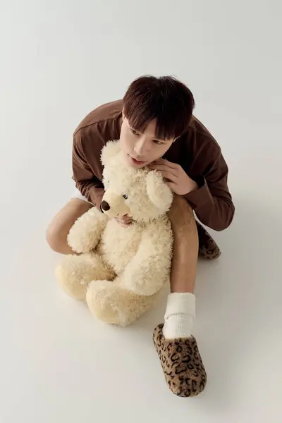 Un jeune homme séduisant tient un ours en peluche moelleux, apportant chaleur et innocence dans un cadre serein. — Photo de stock