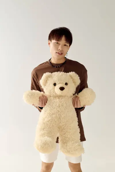Dans un studio lumineux, un bel homme asiatique sourit, embrassant un grand ours en peluche. — Photo de stock
