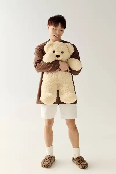 Charming young man in casual attire smiles while holding a soft teddy bear in a light filled space. — Stock Photo