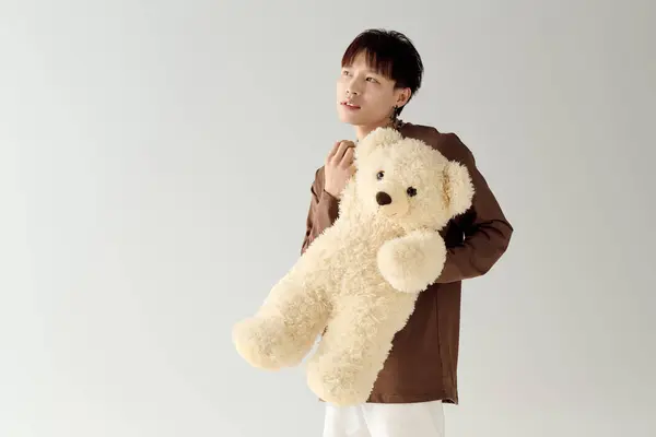Un jeune homme asiatique séduisant embrasse un ours en peluche tout en se tenant debout sur un fond neutre. — Photo de stock