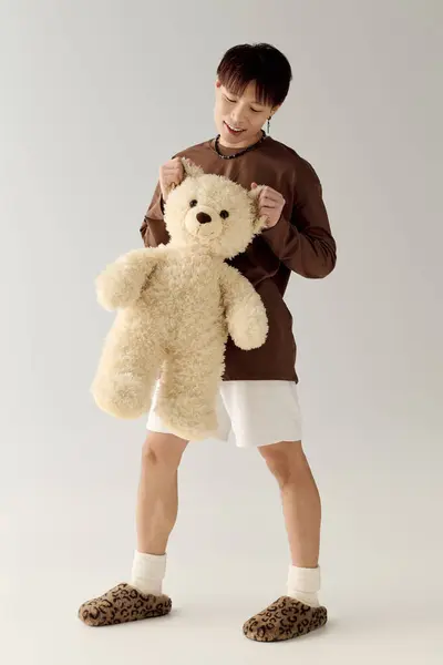 A young, handsome Asian man joyfully holds a fluffy teddy bear in a bright studio. — Stock Photo