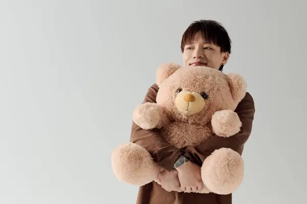 Lumineux et joyeux jeune homme tient un ours en peluche avec un sourire chaleureux dans un studio serein. — Photo de stock