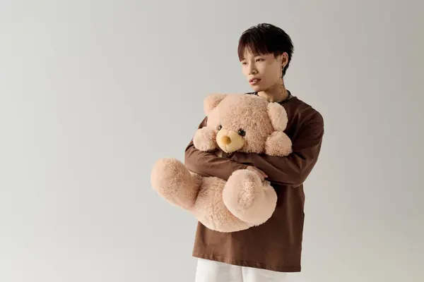Un beau jeune homme embrasse un ours en peluche, rayonnant de chaleur dans un cadre minimaliste. — Photo de stock