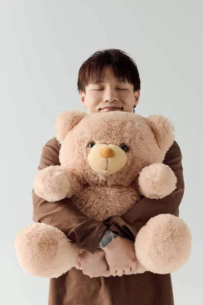 A young man smiles while hugging a large, fluffy teddy bear, exuding warmth and joy. — Stock Photo