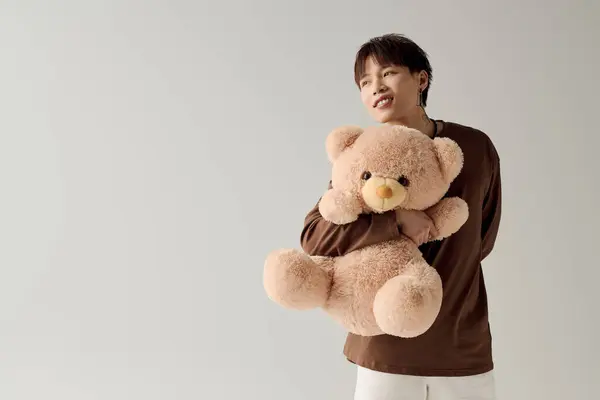 A young Asian man smiles warmly as he hugs a fluffy teddy bear in a bright setting. — Stock Photo