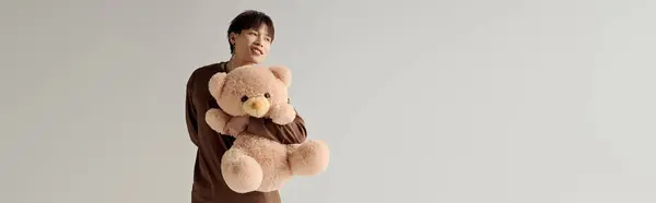 A lively young asian man radiates joy holding a soft teddy bear in a well lit indoor space. — Stock Photo