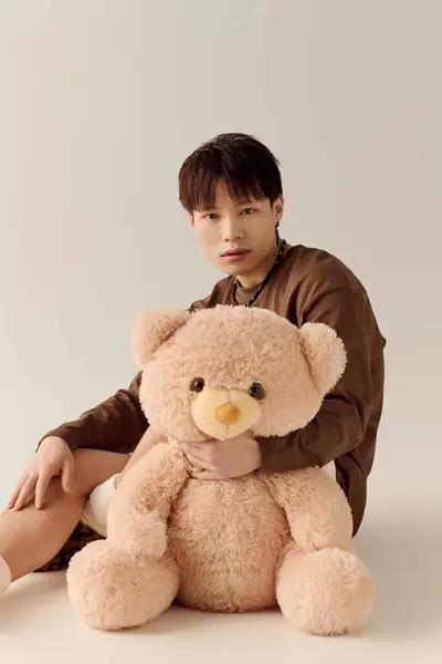 Charmant jeune homme tient doucement un ours en peluche tout en étant assis dans une pièce chaleureuse et accueillante. — Photo de stock