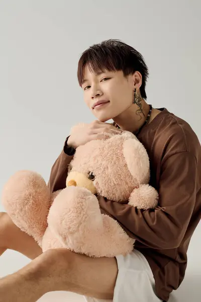 Un jeune asiatique en tenue décontractée câline un ours en peluche moelleux, rayonnant de chaleur. — Photo de stock