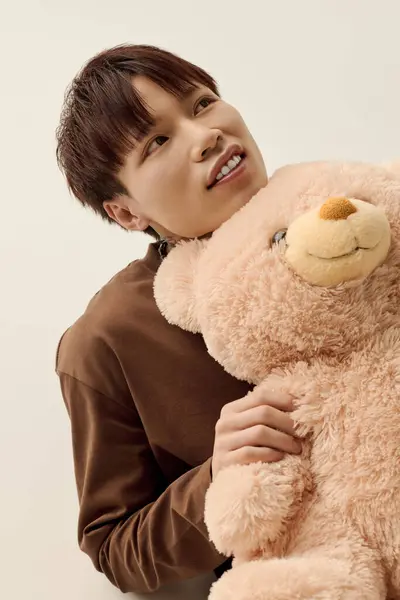 A charming young man embraces a fluffy teddy bear, exuding warmth and happiness in a serene room. — Stock Photo
